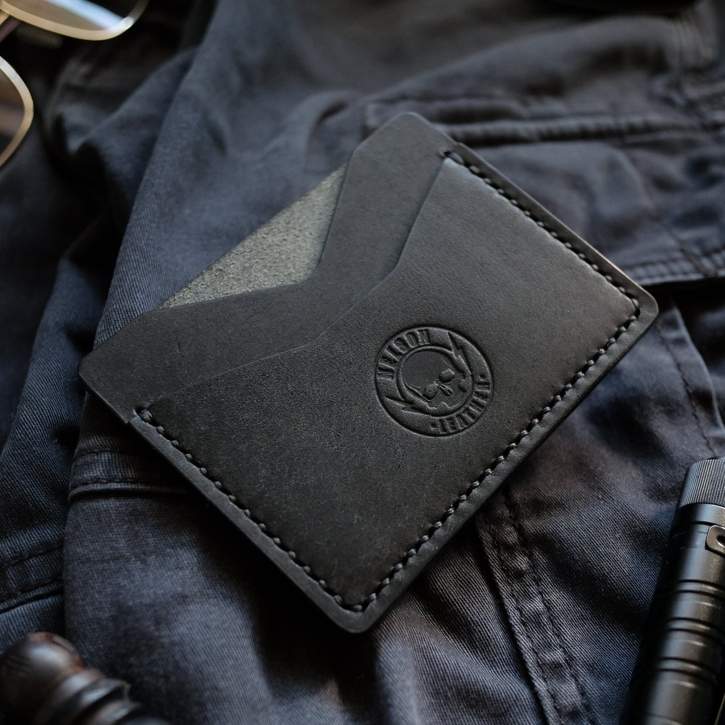 Black leather wallet with a brand logo on a dark fabric background